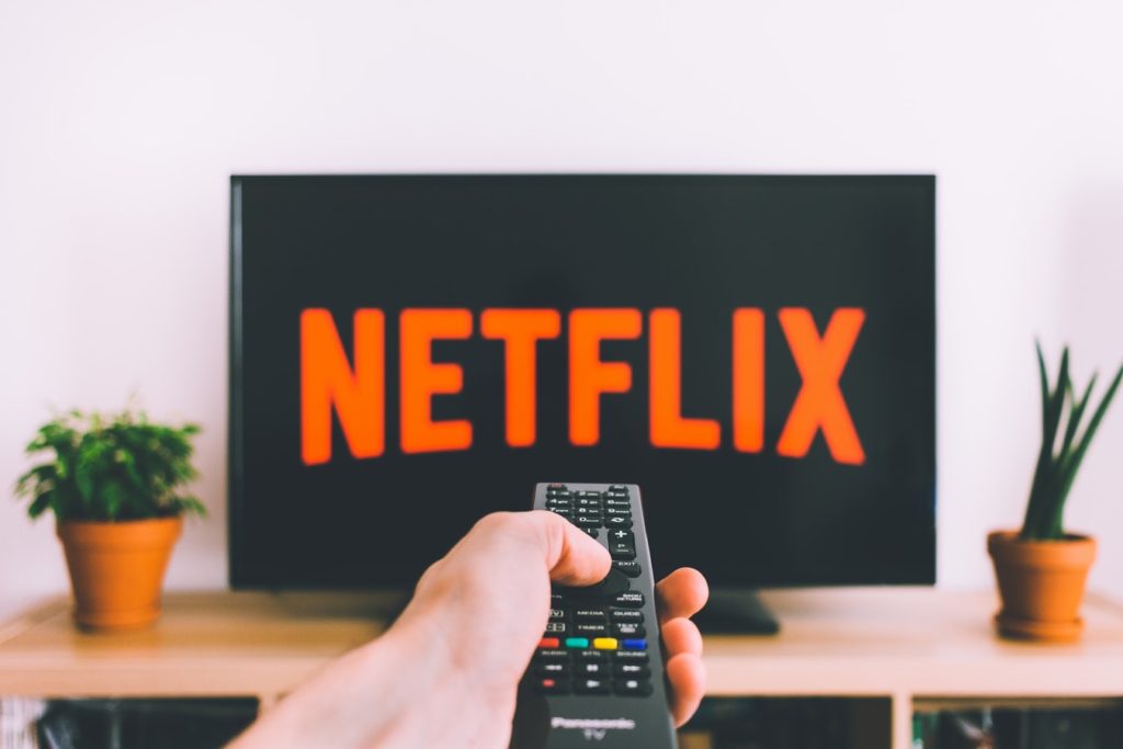 The Netflix title screen displayed on a TV as a hand holds a remote
