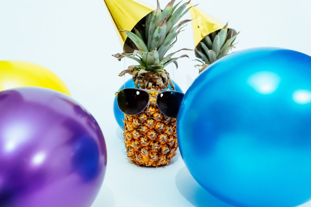pineapple wearing sunglasses surrounded by balloons